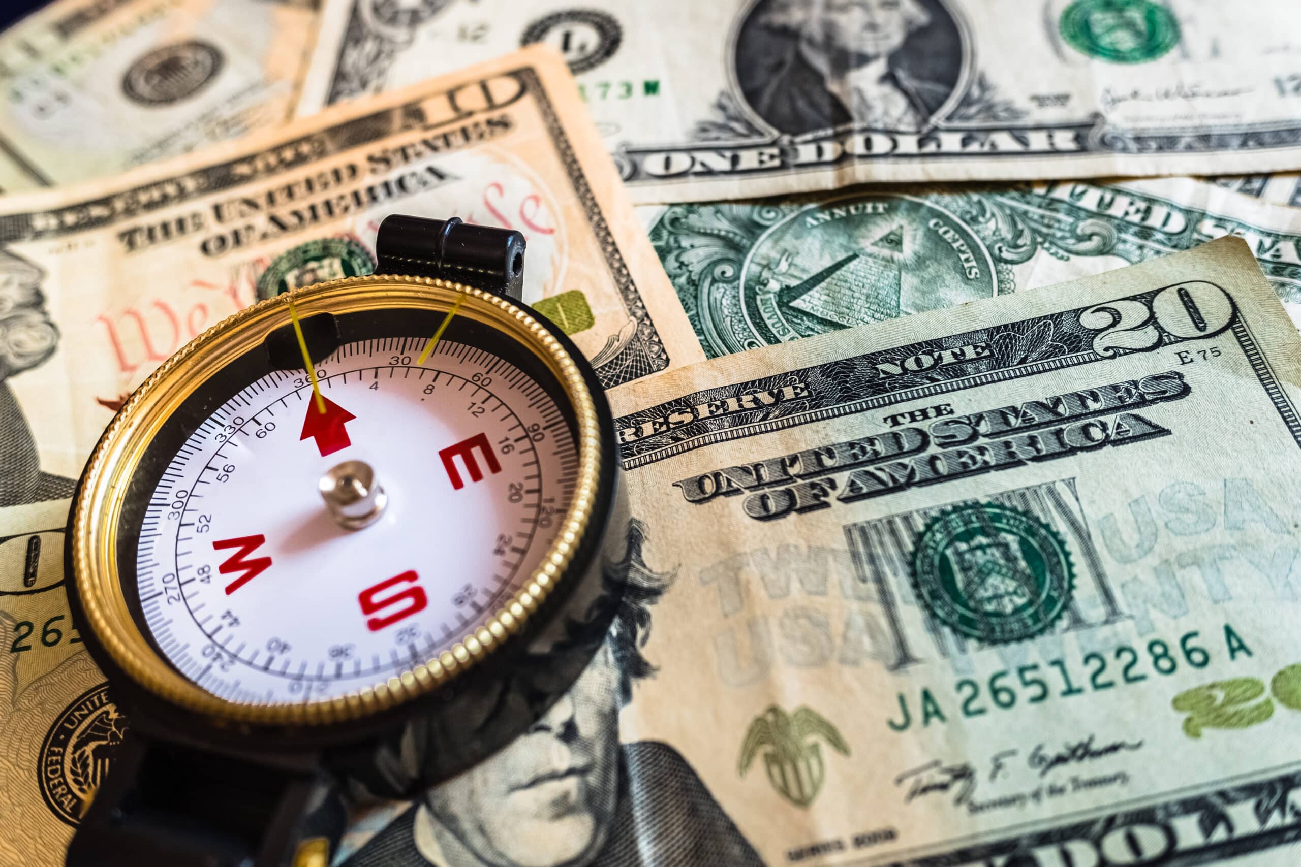 Close-up of a compass on dollar bills, guide for making smart investment decisions.